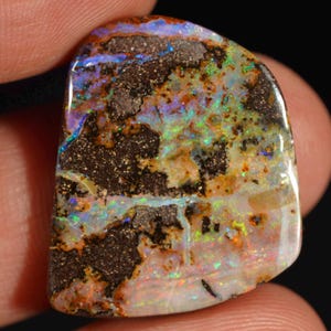 Op de afbeelding: Een gepolijste boulder-opaal edelsteen met een donkerbruine ijzersteenmatrix met levendige flitsen van iriserende blauwe, groene en oranje kleuren over het oppervlak. De steen heeft een onregelmatige, afgeronde vorm met een gladde, glanzende afwerking.