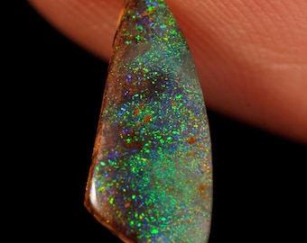 May include: A polished, teardrop-shaped boulder opal gemstone featuring a dark brown ironstone matrix base with vibrant, iridescent flashes of green, blue, and purple color play across its smooth, reflective surface.