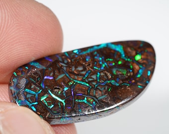 Puede incluir: Una piedra preciosa de ópalo pulida, de forma ovalada. El ópalo muestra un color base marrón oscuro con vibrantes destellos de azul, verde y púrpura. La superficie de la piedra tiene un patrón único, similar a una telaraña, creando un efecto visual llamativo.