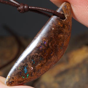 May include: A brown and silver opal pendant with a crescent shape, hanging from a brown leather cord.