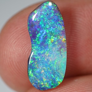 May include: A polished, elongated opal gemstone with a vibrant display of color. The opal features a mix of blues, greens, and purples, with a glossy surface. The gemstone is held between two fingers, showcasing its natural beauty.