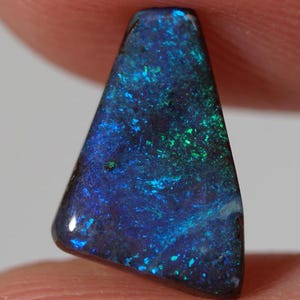 Könnte beinhalten: Ein dunkelblauer und grüner Opal-Edelstein in dreieckiger Form. Der Opal hat eine schimmernde, irisierende Oberfläche.