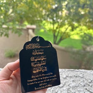 May include: Black rectangular tag with gold Arabic script and English text. The text reads "Glory unto Him Who created this transportation, for us, and we were unable to create it on our own. And unto our Lord, we shall return."