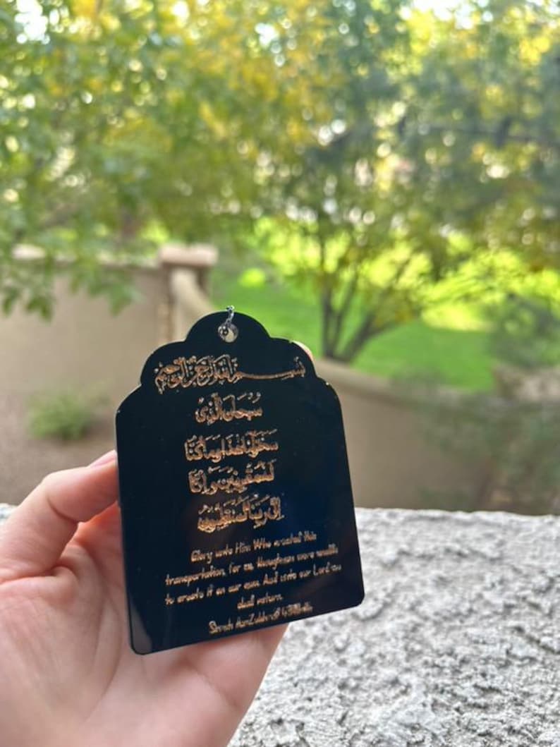 May include: Black rectangular tag with gold Arabic script and English text. The text reads "Glory unto Him Who created this transportation, for us, and we were unable to create it on our own. And unto our Lord, we shall return."