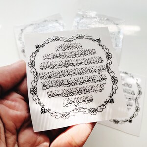 Może przedstawiać: Biała naklejka z ozdobną czarną ramką i arabskim tekstem w srebrnym kolorze. Tekst brzmi: "Bismillah ir-Rahman ir-Rahim, Allah hu al-ilah illa hu al-haiy al-qayyum, laa ta'khuzuhu sinatu wa laa nau, lahu ma fi al-samaawaati wa ma fi al-ard, man dhalika alladhi yashfa'u 'inda al-rahiim illa bi-idhn, ya'lamu ma baina aidihim wa ma khalfahum wa laa yuhiituna bi-shai'in min 'ilmihi illa bi-ma shaa, wasi'a kursiyyuhu al-samaawaati wa al-ard, wa laa ya'uduhu hifdhuhuma wa huwal-'aliyyu al-'azim".