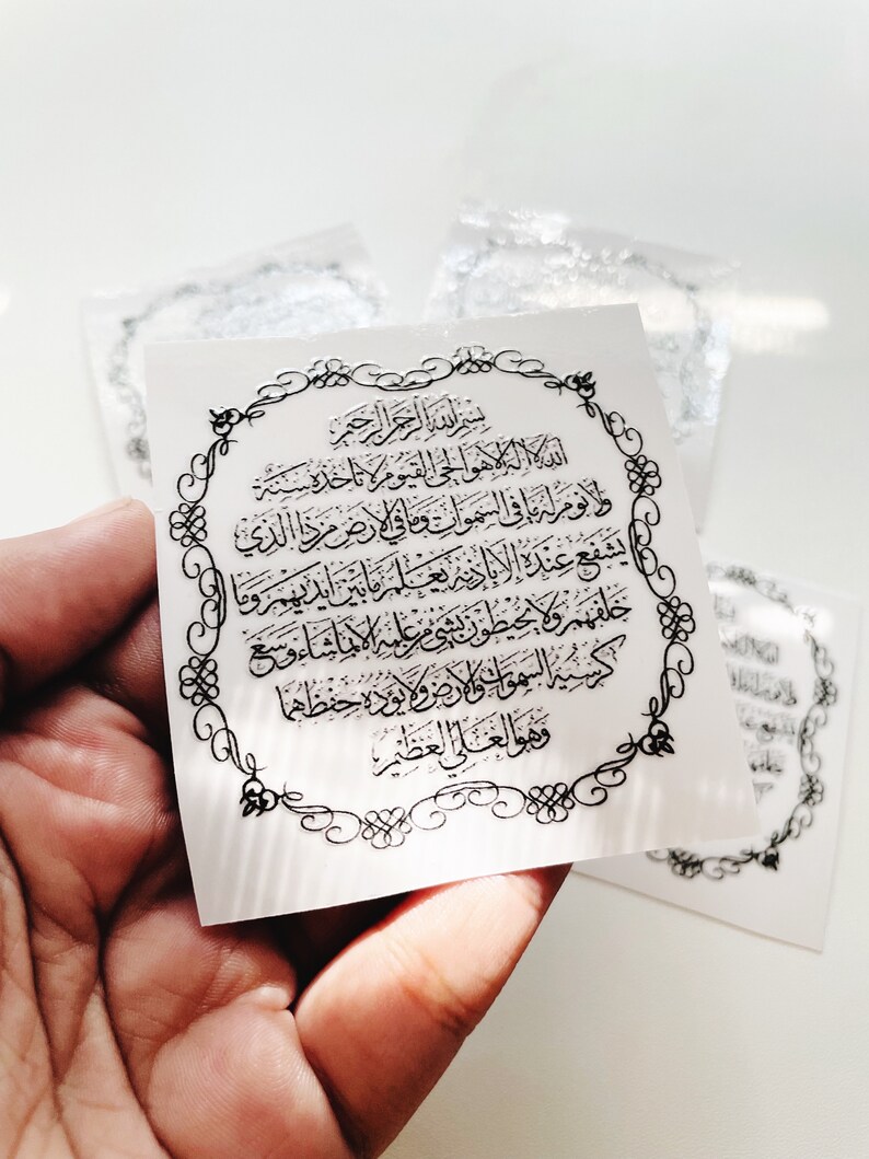 Może przedstawiać: Biała naklejka z ozdobną czarną ramką i arabskim tekstem w srebrnym kolorze. Tekst brzmi: "Bismillah ir-Rahman ir-Rahim, Allah hu al-ilah illa hu al-haiy al-qayyum, laa ta'khuzuhu sinatu wa laa nau, lahu ma fi al-samaawaati wa ma fi al-ard, man dhalika alladhi yashfa'u 'inda al-rahiim illa bi-idhn, ya'lamu ma baina aidihim wa ma khalfahum wa laa yuhiituna bi-shai'in min 'ilmihi illa bi-ma shaa, wasi'a kursiyyuhu al-samaawaati wa al-ard, wa laa ya'uduhu hifdhuhuma wa huwal-'aliyyu al-'azim".