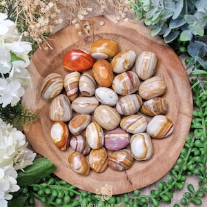 Puede incluir: Una colección de piedras de ágata bandeada pulidas en una variedad de colores, incluyendo marrón, blanco, naranja y rojo. Las piedras son lisas y pulidas, y están dispuestas en un cuenco de madera.