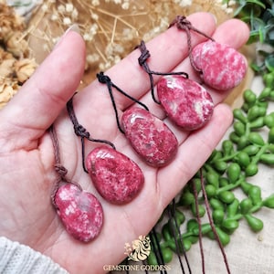 May include: Four polished, irregular, deep pink and white mottled gemstone pendants, each suspended from a thin, dark brown cord with a simple adjustable sliding knot mechanism, showcasing natural stone textures and glossy surfaces.