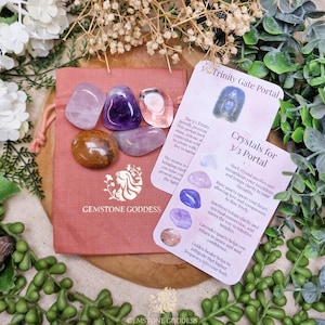 May include: A collection of polished gemstones in various colors, including pink, purple, and brown, are displayed on a pink drawstring bag. Two cards with text are also present, along with decorative greenery. The bag has the text "GEMSTONE GODDESS".