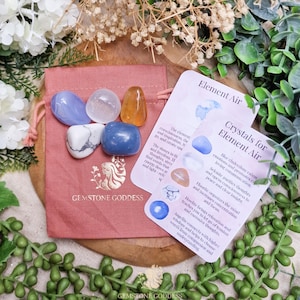 May include: A selection of polished gemstones in shades of blue, orange, and white, presented in a pink pouch. The pouch is printed with the text "GEMSTONE GODDESS". Two cards with text are also visible.