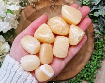 May include: A collection of tumbled yellow calcite stones, also known as honey calcite, in various sizes and shapes. The stones are smooth and polished, with a warm, honey-like color.