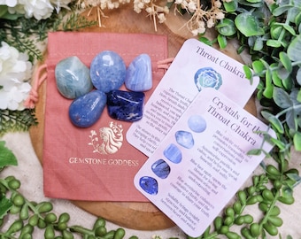 May include: A collection of blue gemstones in various shapes and shades, including aquamarine and sodalite, presented in a pink drawstring bag. Accompanying cards detail the Throat Chakra and crystal properties. The text "GEMSTONE GODDESS" is visible.