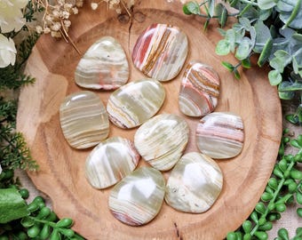 May include: A collection of ten polished green, white, and brown onyx stones. The stones are smooth and have a natural, organic shape. They are arranged on a wooden surface.