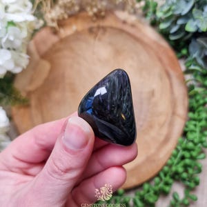 May include: A dark blue and black gemstone with a triangular shape. The gemstone has a smooth, polished surface and a shimmering, iridescent effect.