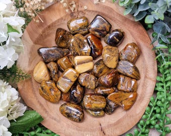 May include: A collection of tumbled tiger's eye stones in various shades of brown and gold. The stones are smooth and polished, with a natural, earthy look.