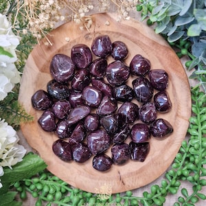 Puede incluir: Una colección de piedras de granate rojo pulidas en un cuenco de madera. Las piedras son lisas y pulidas, de un color rojo intenso.