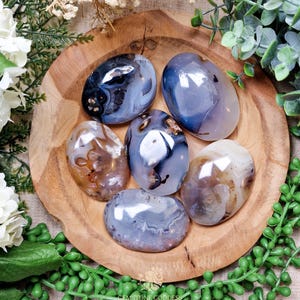 May include: Six smooth, polished agate stones in various shades of blue, brown, and white. The stones are arranged on a wooden surface.