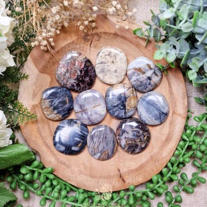 Peut inclure: Une collection de neuf pierres de paume rondes et polies en pierre naturelle. Les pierres sont de différentes nuances de gris, de brun et de blanc avec des motifs complexes.