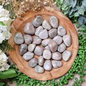 May include: A bowl of tumbled grey and white banded agate stones. The stones are smooth and polished, with a variety of patterns and colors.