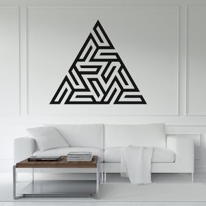 Puede incluir: Una gran obra de arte mural triangular geométrica negra con un intrincado diseño en forma de laberinto. La obra de arte está montada en una pared blanca sobre un sofá blanco y una mesa de centro de madera.