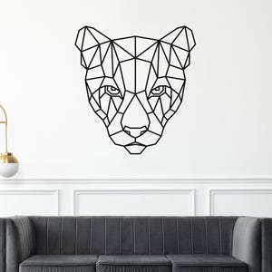May include: A black geometric wall art piece depicting a cheetah's head. The artwork is composed of interconnected straight lines, creating a low-poly design. The cheetah's face is centered, with visible eyes, nose, and ears. The art is mounted on a white wall.