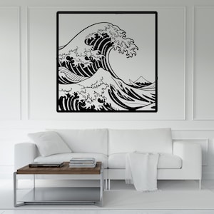 May include: Black and white wall art featuring a stylized depiction of a large ocean wave, with intricate details in the cresting water. The artwork is framed in a black border and mounted on a white wall, above a white sofa and a wooden coffee table.