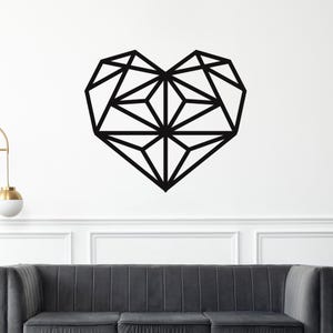 May include: A black geometric heart wall art piece. The heart is composed of interconnected lines and shapes, creating a modern, angular design. The artwork is mounted on a white wall above a gray sofa, adding a touch of contemporary style to the room.