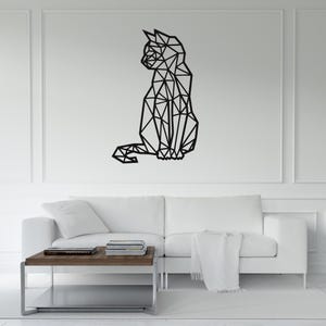 May include: A black geometric cat wall art piece. The cat is depicted in a sitting position, crafted from interconnected triangular shapes. The artwork is mounted on a white wall above a white sofa and a wooden coffee table.