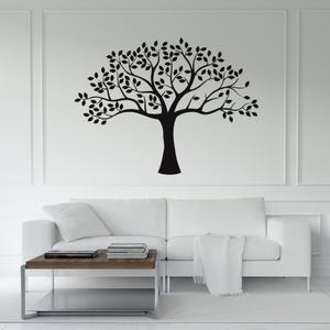 May include: A black tree wall decal with leaves, displayed on a white wall above a white sofa. The tree design is a silhouette, creating a minimalist and modern aesthetic. The room features a coffee table and a white rug.