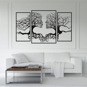 May include: A triptych wall art piece featuring a black tree-like design with human faces intertwined. The artwork is set against a white background, with a white sofa and coffee table in the foreground. The artwork is framed in black.
