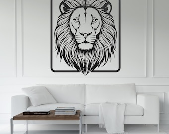 May include: Black and white lion head wall art. The lion's face is centered within a black rectangular frame. The lion's mane is detailed with flowing lines. The artwork is displayed on a white wall above a white sofa and a wooden coffee table.