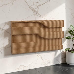 Puede incluir: Un panel de pared rectangular de color beige con un diseño tridimensional en forma de onda. El panel presenta líneas verticales y paralelas y está montado en una pared de mármol blanco. Una planta en maceta es visible a la derecha.