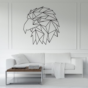 May include: Geometric black eagle head wall art. The eagle's head is composed of angular shapes, creating a modern, minimalist design. The artwork is mounted on a white wall above a white sofa and a wooden coffee table.