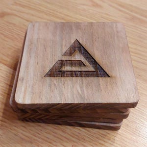 Può includere: Un set di quattro sottobicchieri in legno con un design a triangolo geometrico. I sottobicchieri sono realizzati in legno scuro e hanno una finitura naturale.
