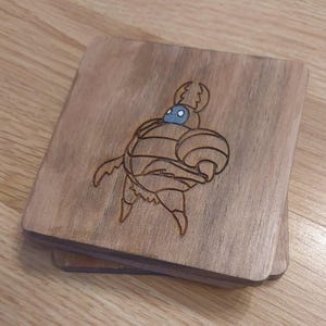 Peut inclure: Ensemble de quatre sous-verres en bois avec un motif gravé au laser d'un chevalier du jeu vidéo Hollow Knight. Le chevalier porte une armure et un casque avec un seul œil.