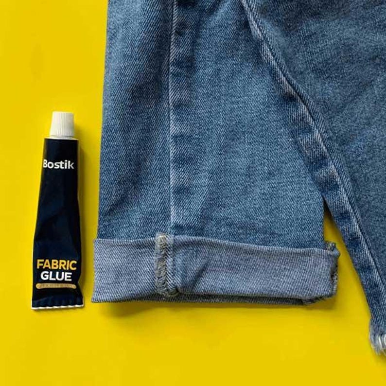 May include: A tube of Bostik Fabric Glue on a yellow background. The glue is black with white lettering that says "Bostik Fabric Glue".