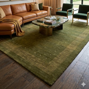 Puede incluir: Un salón lujoso con un sofá seccional de cuero marrón, dos sillones verdes y una alfombra verde con un borde dorado punteado. Una mesa de centro única con una tapa de piedra verde se encuentra en el centro. Una gran pintura abstracta cuelga en la pared.