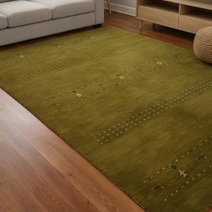 May include: A large olive green area rug with a subtle pattern of dotted lines and small decorative elements. The rug is placed in a living room setting with a sofa, side table, and entertainment center.