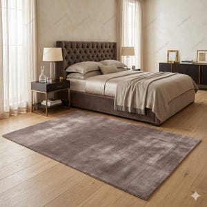 May include: A bedroom scene featuring a large bed with a tufted headboard, neutral-toned bedding, and a matching throw blanket. A large, rectangular, brown rug sits on the wooden floor. Two bedside tables with lamps and a dark dresser complete the room.