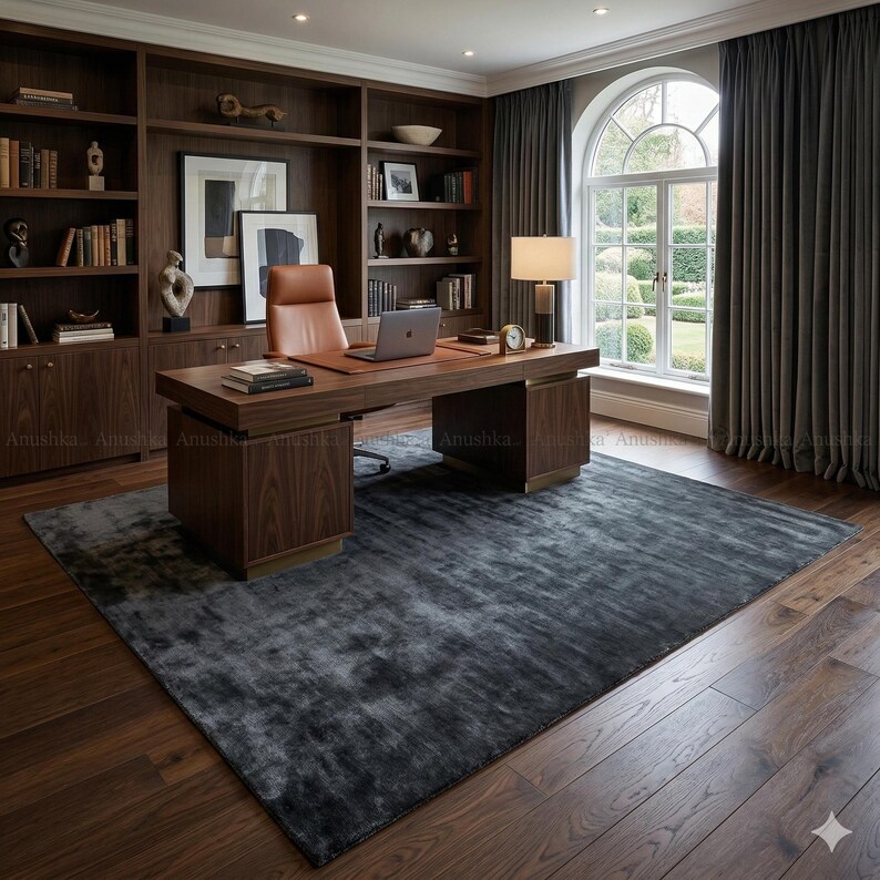 May include: A luxurious home office featuring a dark wood desk with a leather top, a matching bookcase, and a gray rug. The room includes a laptop, a desk lamp, and a leather office chair. The large window is draped with dark gray curtains.