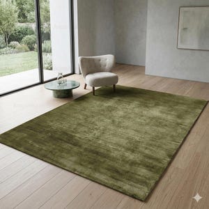May include: A large, rectangular olive green rug dominates the room. The rug has a textured appearance and covers a significant portion of the light-colored wooden floor. A small, round green marble table and a cream-colored armchair are also visible.