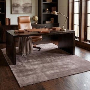 May include: A home office setup featuring a dark wood desk, a brown leather chair, and a matching desk pad. A tan throw blanket is draped over the chair. A rug in shades of gray and brown covers the floor. A brass desk lamp and globe are visible.