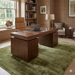 May include: A modern office setting featuring a large, dark wood desk with a built-in leather top and a laptop. A tan leather office chair sits behind the desk. The room has a green rug and a bookshelf.