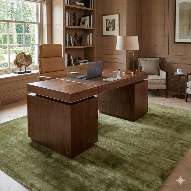 May include: A modern office setting featuring a large, dark wood desk with a built-in leather top and a laptop. A tan leather office chair sits behind the desk. The room has a green rug and a bookshelf.