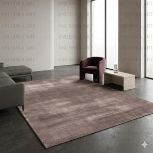 May include: A large, rectangular, brown area rug with a subtle pattern dominates the room. A dark purple armchair and a light-colored wooden coffee table are placed near a large window. The words "ANUSHKA ART" are repeated across the image.