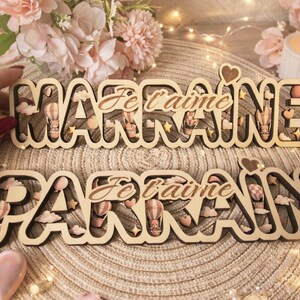 Peut inclure: Deux panneaux en bois avec les mots "Marraine" et "Parrain" dans une police décorative, chacun avec la phrase "Je t'aime" au centre. Les panneaux sont décorés de montgolfières, de nuages et d'étoiles. Les panneaux sont en bois clair.