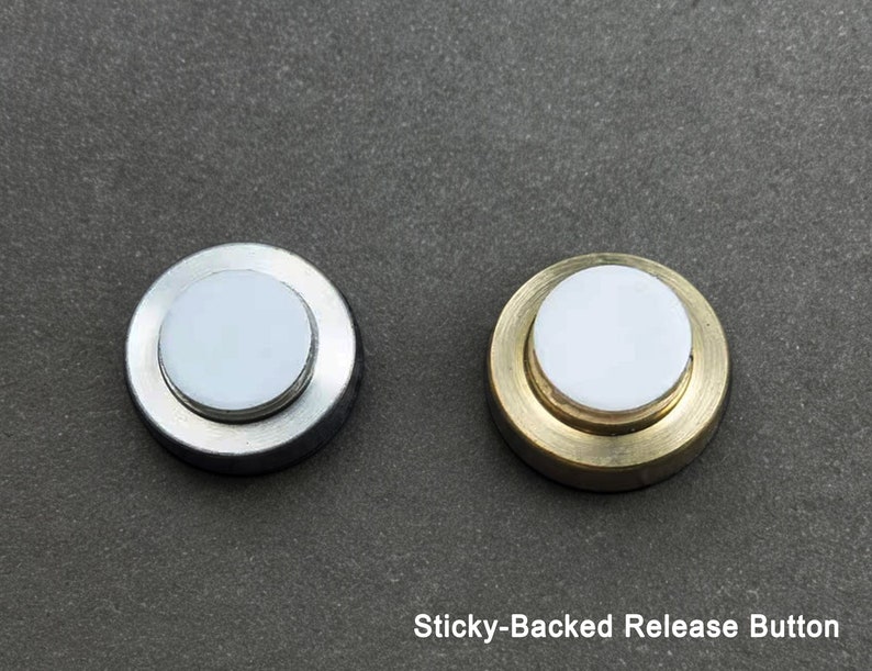 May include: Two sticky-backed release buttons, one with a silver finish and one with a gold finish.  The buttons are round and have a white center.
