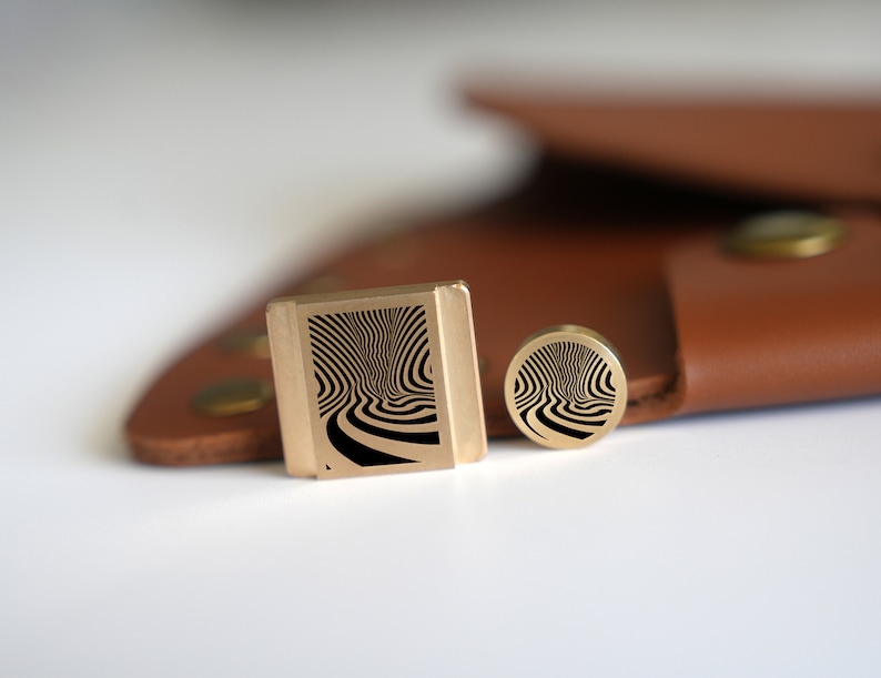 May include: Two brass stamp designs with a black and white swirl pattern. The larger stamp is rectangular and the smaller stamp is round.