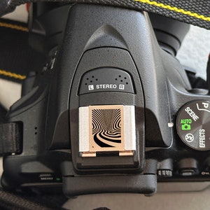 May include: A black digital camera with a silver hot shoe and a black and white patterned flash diffuser. The camera has a mode dial with the following settings: P, S, A, M, and Auto. The camera also has a scene mode dial with the following settings: Portrait, Landscape, Sports, Night Portrait, and Macro.