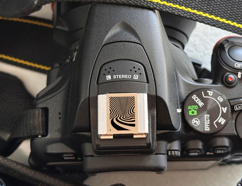 May include: A black digital camera with a silver hot shoe and a black and white patterned flash diffuser. The camera has a mode dial with the following settings: P, S, A, M, and Auto. The camera also has a scene mode dial with the following settings: Portrait, Landscape, Sports, Night Portrait, and Macro.